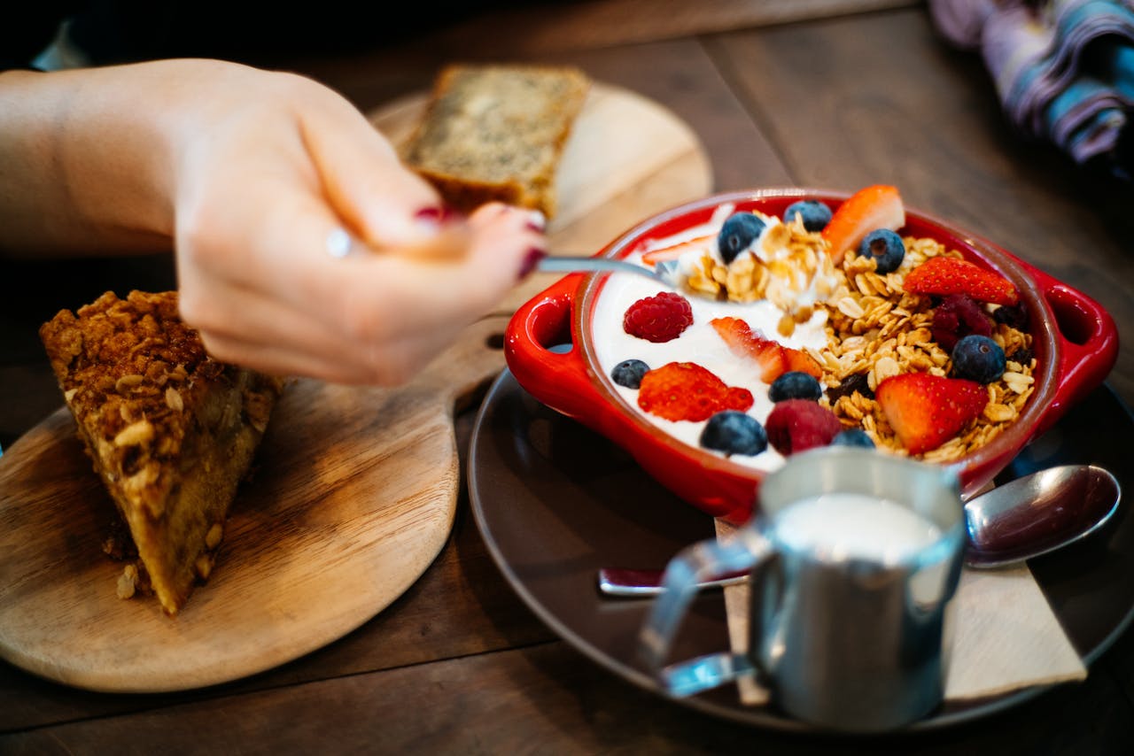our-services-02 Close-up of a breakfast setting with granola, fresh berries, and a slice of cake.